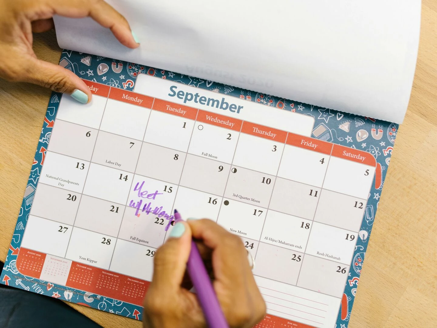 a person marking a calendar in september with a purple pen on a wooden desk