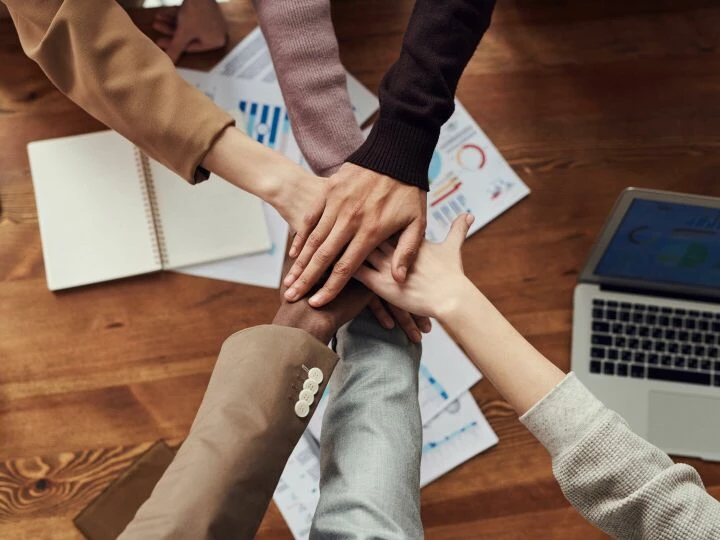 Diverse professionals unite for teamwork around a wooden table with laptops and documents.