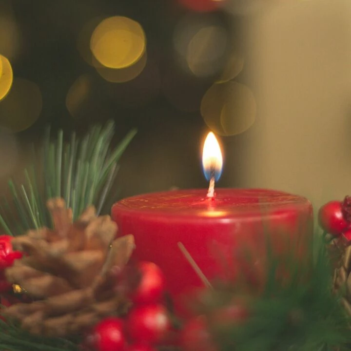 Red candle with pine cones and blurred bokeh lights, perfect for holiday decor inspiration.