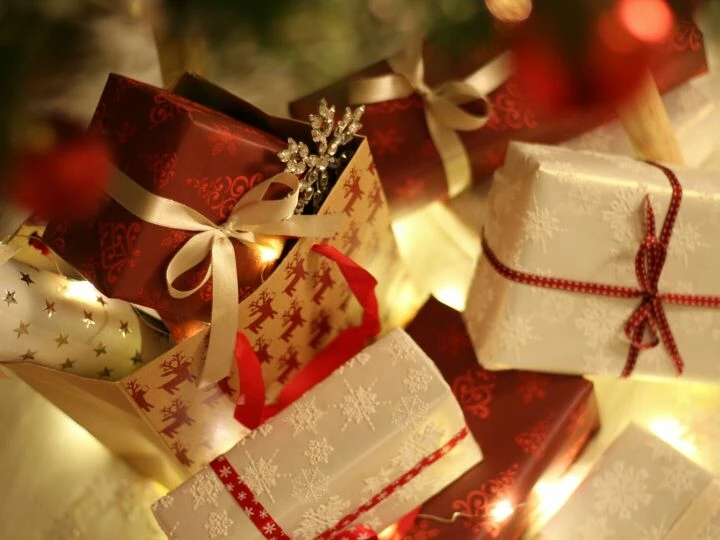 Beautifully wrapped Christmas presents under the tree with festive decorations and ribbons.