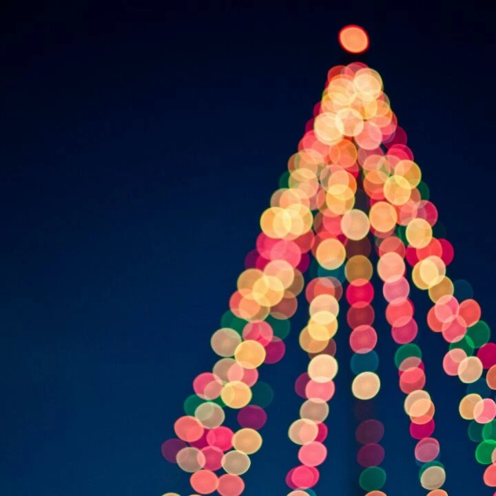 Colorful bokeh lights forming a Christmas tree against a dark blue sky.