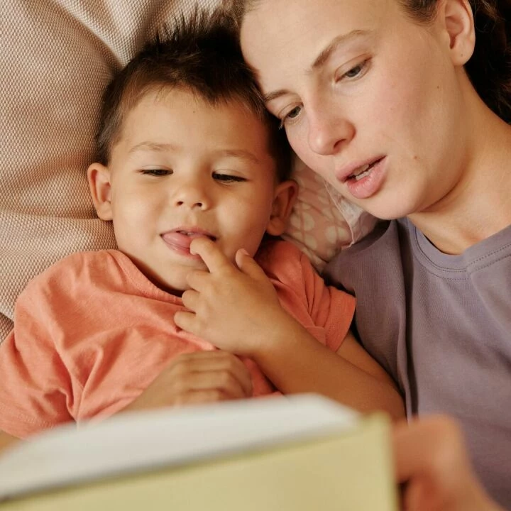 A loving mother and her young son enjoy reading a book together in bed. Captured in a cozy home setting.
