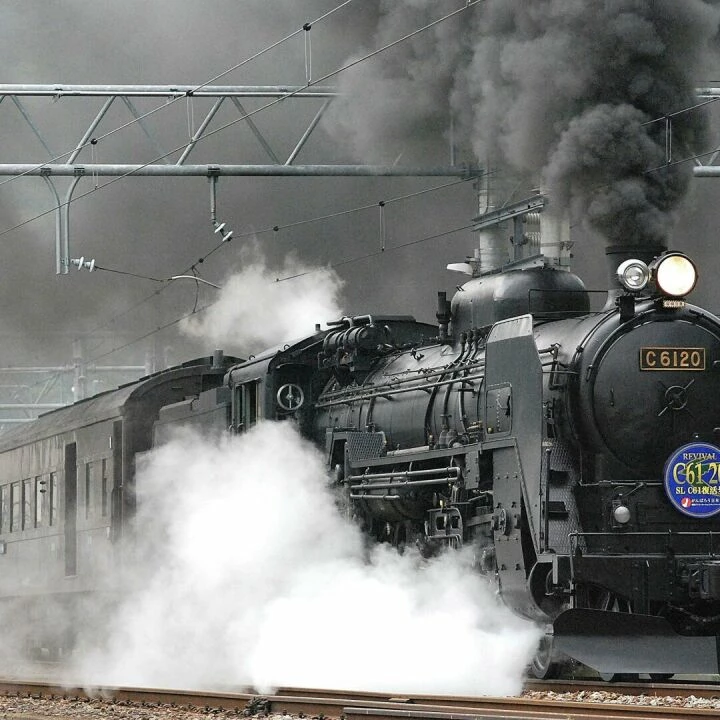 Steam locomotive releasing smoke and steam on a rail track, showcasing vintage train transportation.