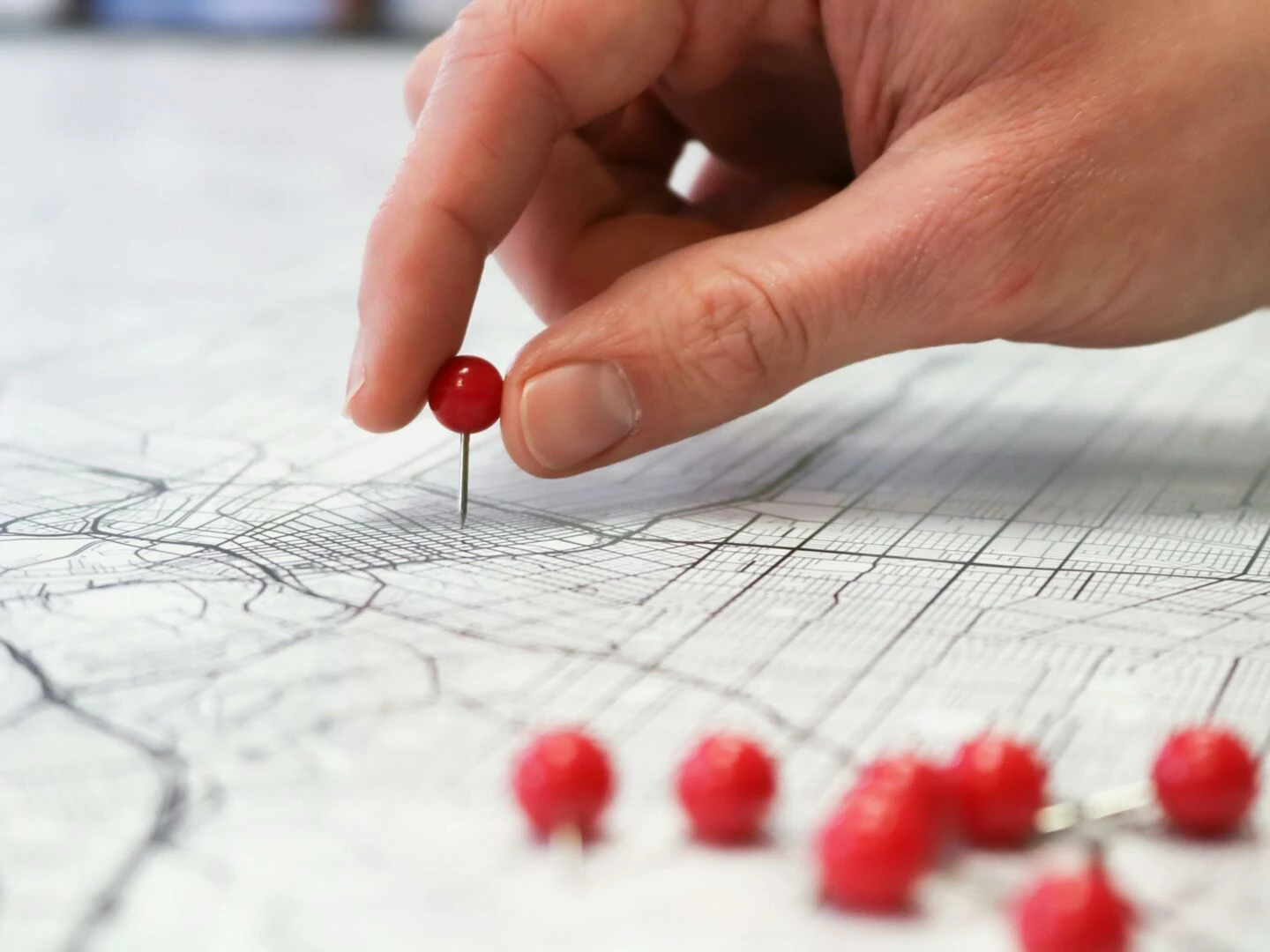 closeup of a hand placing a red pin on a map indicating geographic location pinning