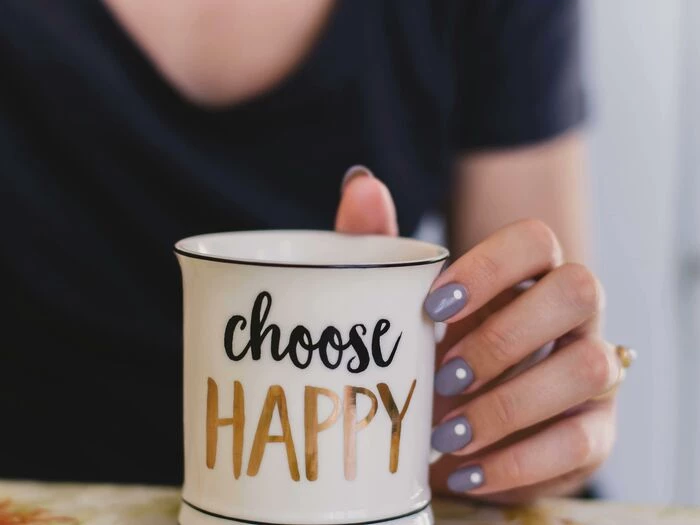 selective focus photography of person touch the white ceramic mug with choose happy graphic