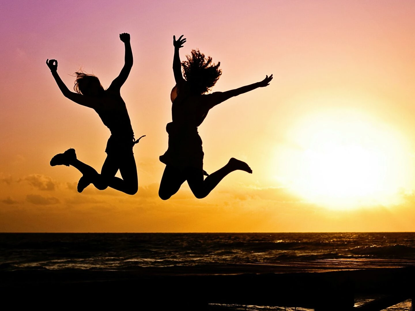 silhouettes of two people joyfully jumping on a beach during a vibrant sunset