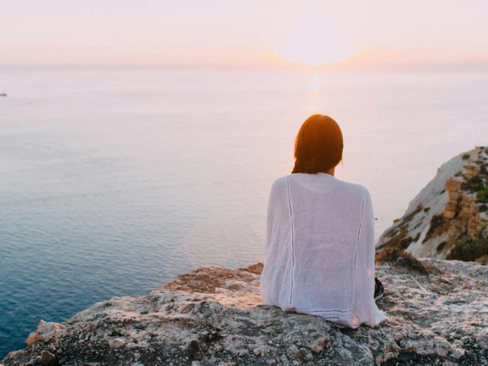 woman sitting on gray rock near body of water